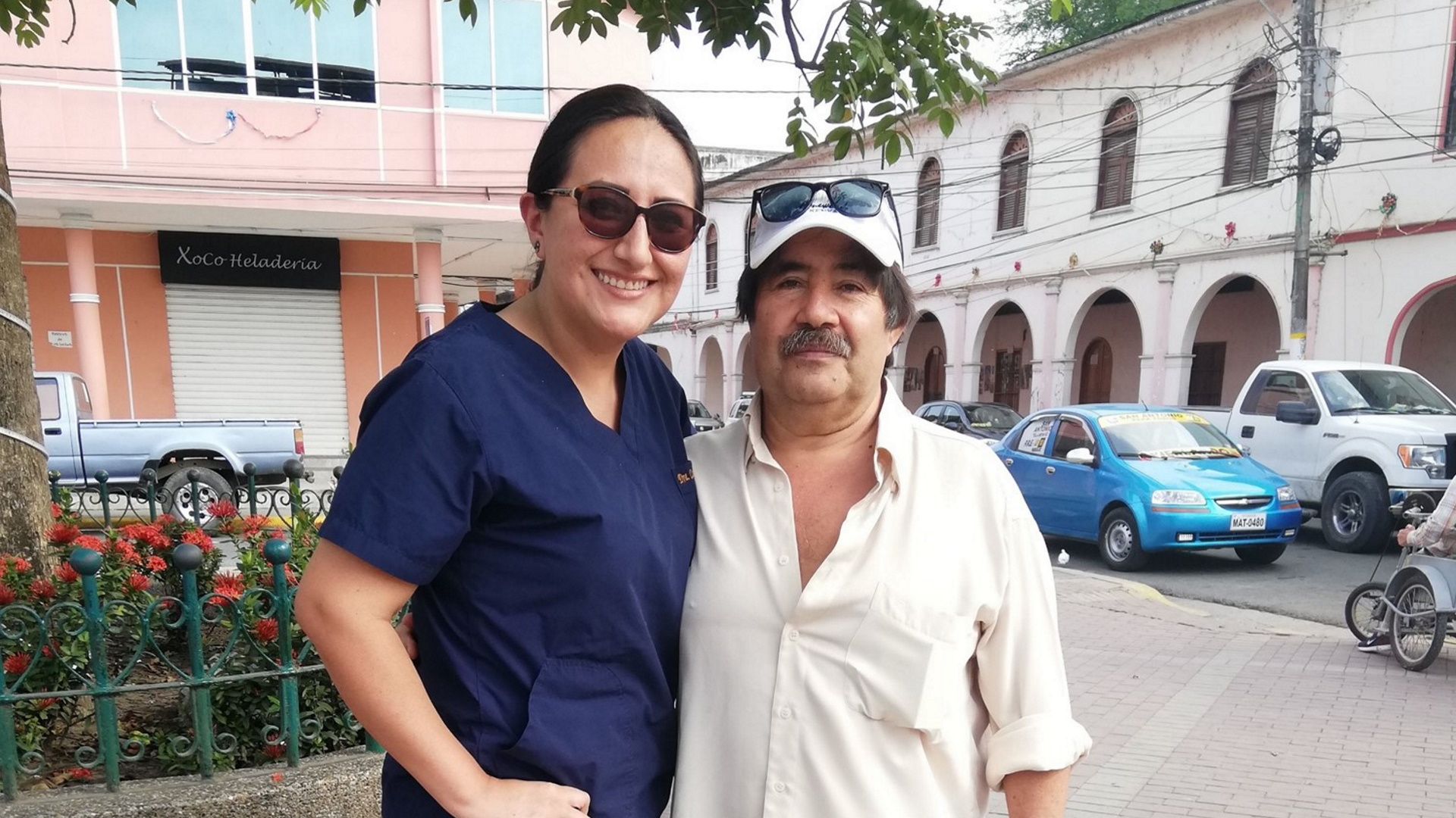 A woman stands smiling next to a man. They are both looking into the camera.